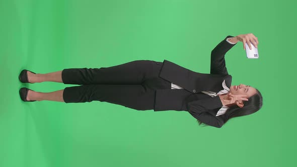 Full Body Of A Smiling Asian Business Woman Making Selfie On Mobile Phone On Green Screen