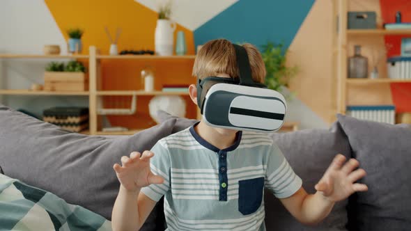 Happy Boy Is Using Virtual Reality Glasses Looking Around Gesturing Sitting in Apartment