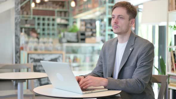 Attractive Young Man Looking at Camera While Using Laptop in Cafe