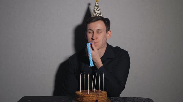 Young Man Celebrates a Holiday, He Sits Alone at a Table with a Cake and a Candles