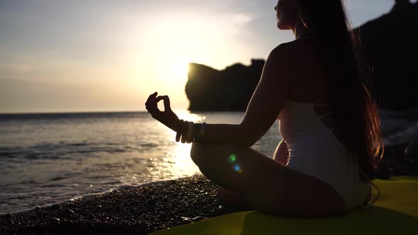 Young Woman with Long Hair Practicing Stretching Outdoors on Yoga Mat By the Sea on a Warm Sunset