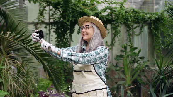 Elderly Woman in Straw Hat and Working Clothes Making Photos on Phone Being