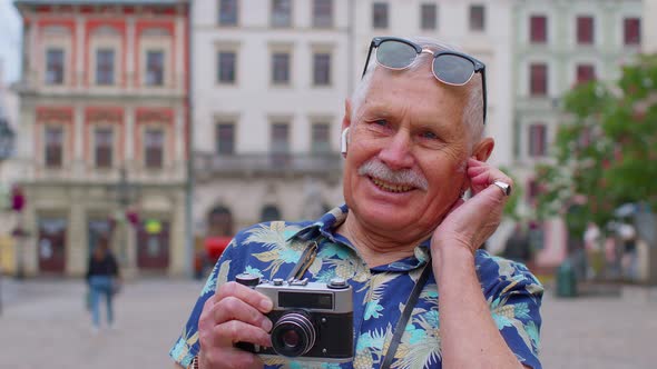 Senior Tourist with Retro Photo Camera Listening to Music on Earphones Dancing Outdoors Having Fun