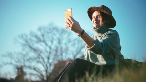 A Beautiful Middleaged Woman in a Hat Is Taking a Video Call on Her Smartphone