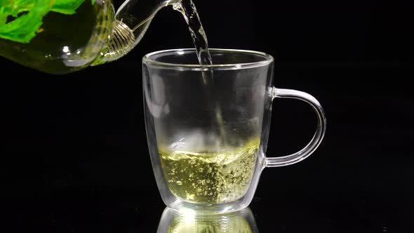 Green Tea Is Being Poured From the Glass Teapot Ona Black Background