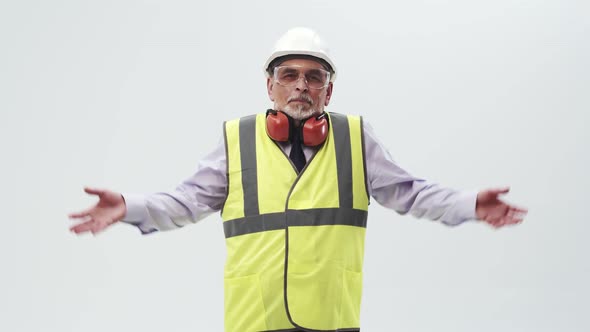 Adult Man Engineer in Confusion Spreads Hands to the Sides Standing in a Vest and Helmet with