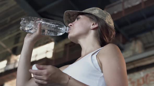 Portrait of Pretty Young Woman in Military Cap Drinking Water From the Bottle in Dusty Dirty