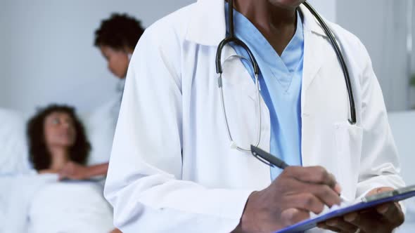 Close-up of African american doctor looking at camera while writing on clipboard in the ward 