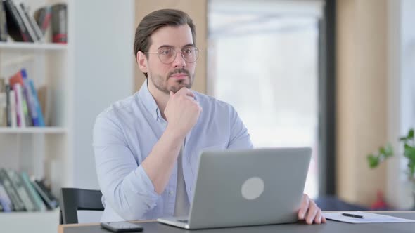 Man in Glasses with Laptop Thinking in Office