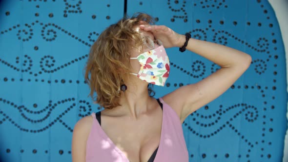 a Young Woman Wearing Glasses and a Protective Mask with a Floral Print Against the Background of