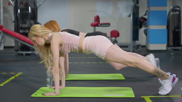 Side View of Slim Fit Caucasian Sportswomen Standing in Plank Position in Gym on Exercise Mat