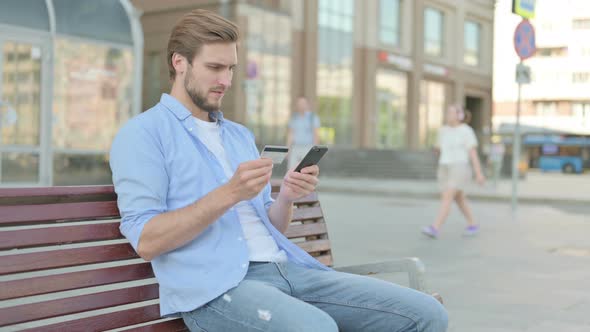 Excited Man Shopping Online Via Smartphone While Sitting Outdoor on Bench