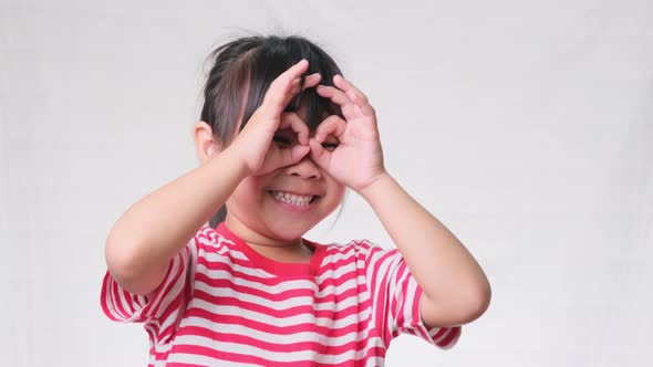Cute little girl making funny faces wearing fingering glasses, shaped like looking through binocular alt