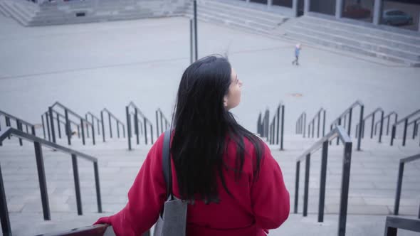 Back View of Elegant Young Lady in Red Coat Walking Down the Stairs. Confident Caucasian Woman with