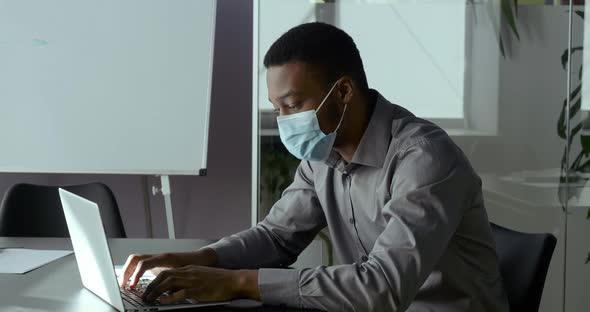 Young African Man Confident Business Man Foreign Student in Medical Protective Mask Typing on Laptop