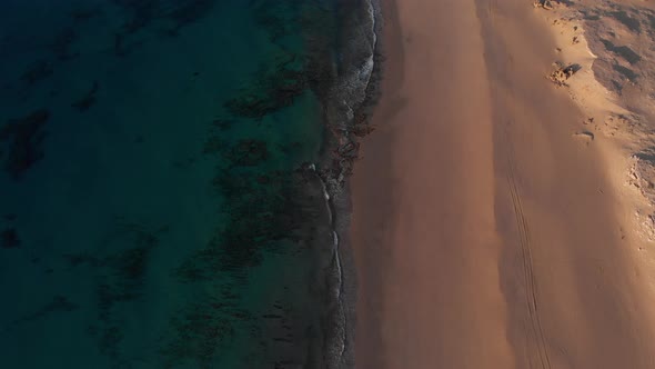 Lockdown aerial view over golden sand and turquoise waters at sunrise. Matadouro