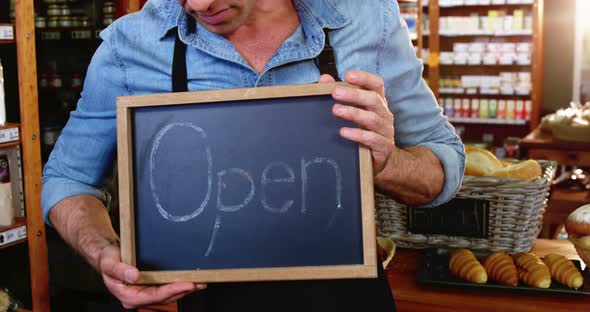 Male staff holding a open sign slate in supermarket