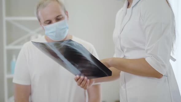 Lungs X-ray in Female Hands with Unrecognizable Doctor Explaining Roentgen To Mid-adult Man in Face