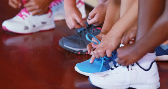 Girls tying shoe laces in basketball court