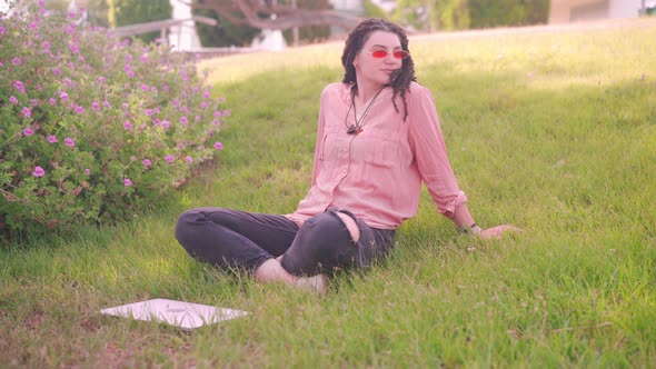 Attractive Woman with Dreadlocks Working at the Laptop Sitting Grass in City Park