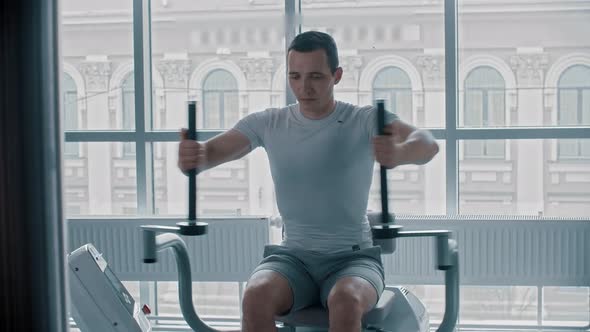 Modern Gym - a Young Guy in White T-shirt Doing Arm Exercise on the Training Apparatus