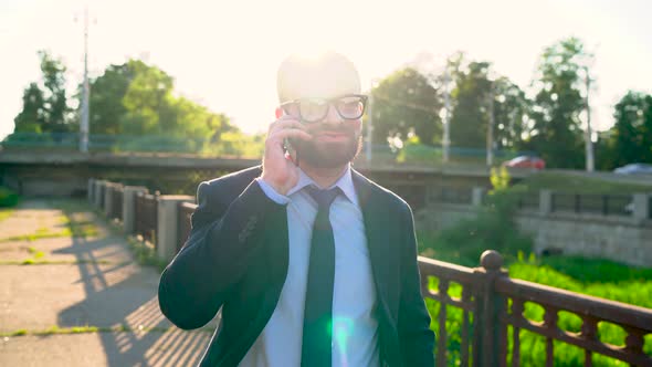 Man Talking on Smartphone and Walking Down the Street at Sunset