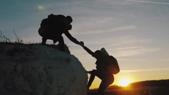 Silhouette of Helping Hand Between Two Climber. Two Hikers on Top of the Mountain, a Man Helps