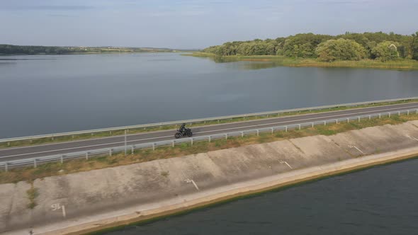 Biker is Driving Motorbike Through Bridge of River on Summer Day