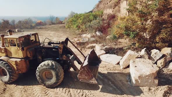 professional bulldozer with a bucket is picking up stones on sand quarry