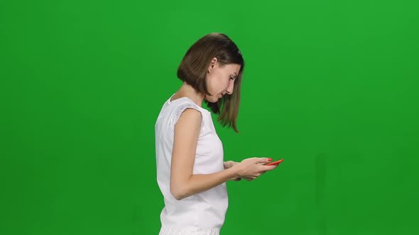 Portrait of Young Woman Is Walking and Texting Message Vie Her Mobile Phone on Green Screen. Profile