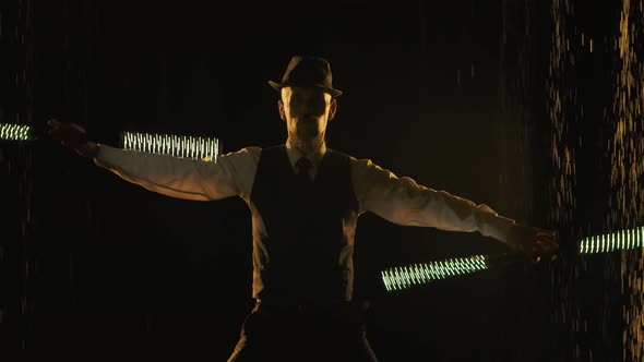 A Young Man Performs Professionally with a Fire Show and Twirls LED Sticks in a Dark Studio