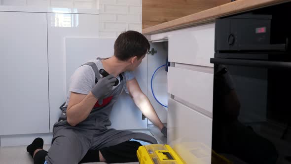 Skilled Craftsman with Flashlight Examines Pipes Under Sink