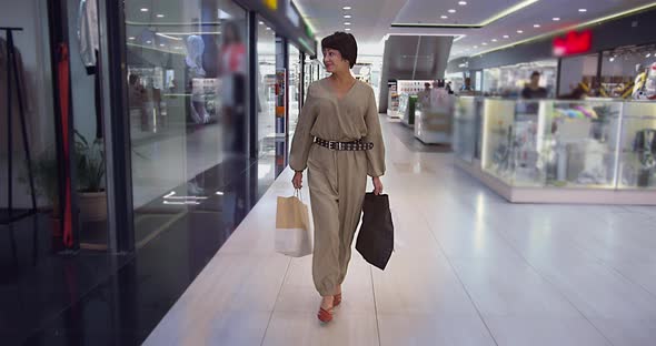 Brunette Woman Walks in the Mall Looking at the Camera Examines Shop Windows Shopping