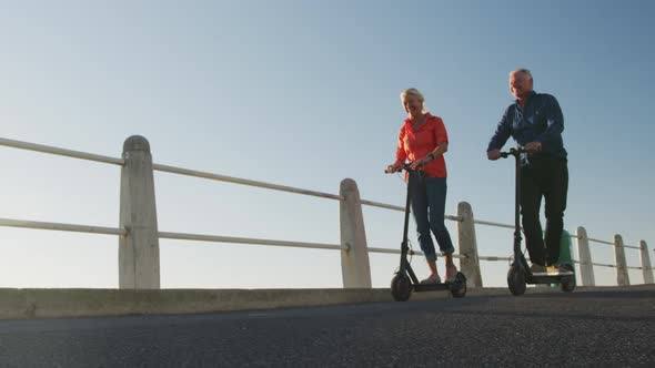 Senior couple using electronic scooters alongside beach