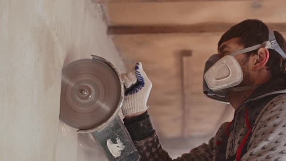 Caucasian Male Worker Wearing Respirator Using Angle Grinder to Cut Wall in Slowmotion