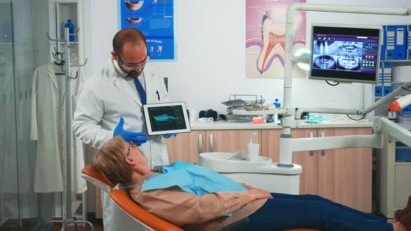 Woman Sitting on Dental Chair Listening Doctor Looking on Tablet