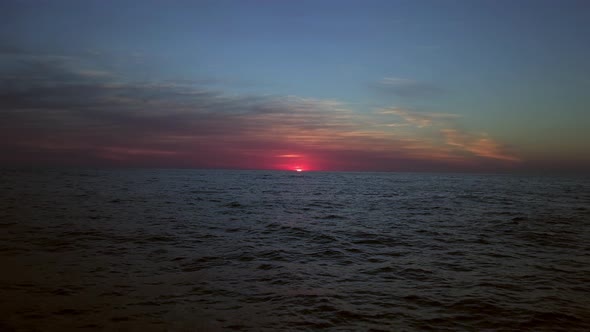 Deep dark blue panoramic ocean view from a drone with a vivid red shining sun. Colorful gloomy sunbe