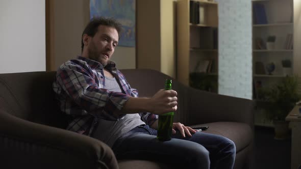 Drunk Male Sitting on Couch and Talking to Bottle of Beer, Addiction to Alcohol