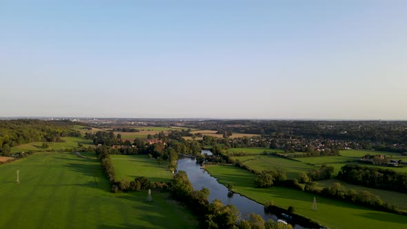 Vibrant green color of river Thames shores and surrounding countryside. Aerial forward