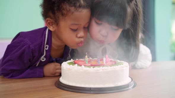 Multi-ethnic young girls happy make a wish blow out candles on birthday cake at school.