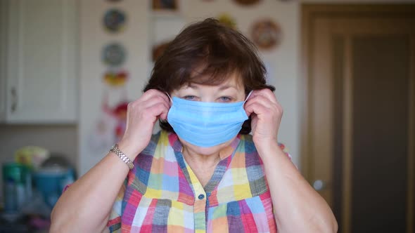 aged woman putting on protective medical mask in her kitchen