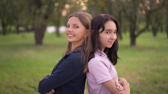 Confident Smiling Teenage Girls Standing Back to Back in Spring Summer Park Looking at Camera