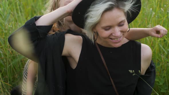 Mother with Two Daughters in Black Dresses Sits on a Field