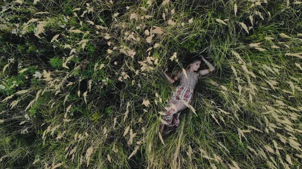 Caucasian Hippie Girl Lying on Her Back in a Field of Dry Grass, Concept of a Child of Nature