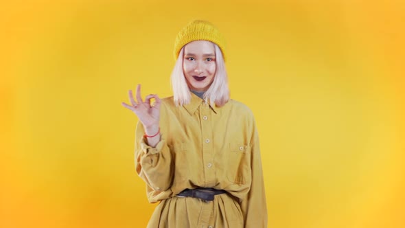 Positive Girl Making OK Sign Over Yellow Background and Smiles To Camera.