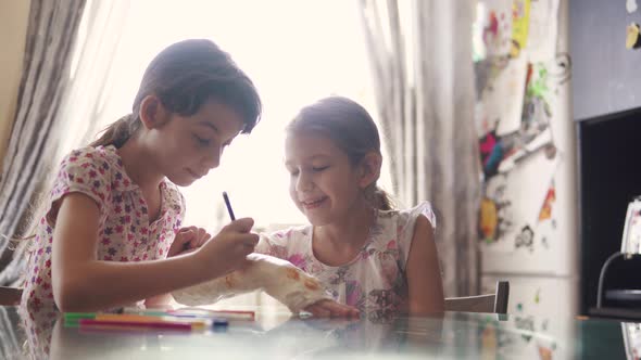 Older Sister Paints a Plastered Hand To Her Younger Sister. Child Cares and Supports His Friend