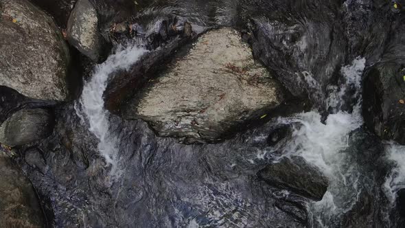 High view of a slowed down creek bed with water flowing between natural coloured rocks