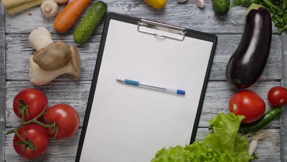 Pen Rolling on Clipboard on Kitchen Table with Vegetables