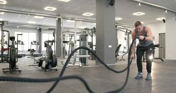 Athletic Guy Focused on Fitness Workout with Ropes in the Gym