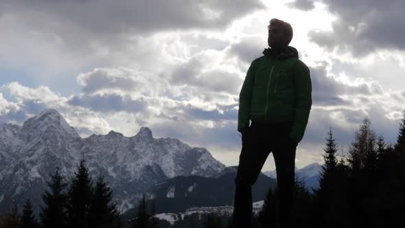 Silhouette of a man standing and looking at the scenic view of clouds and mountains in the winter.